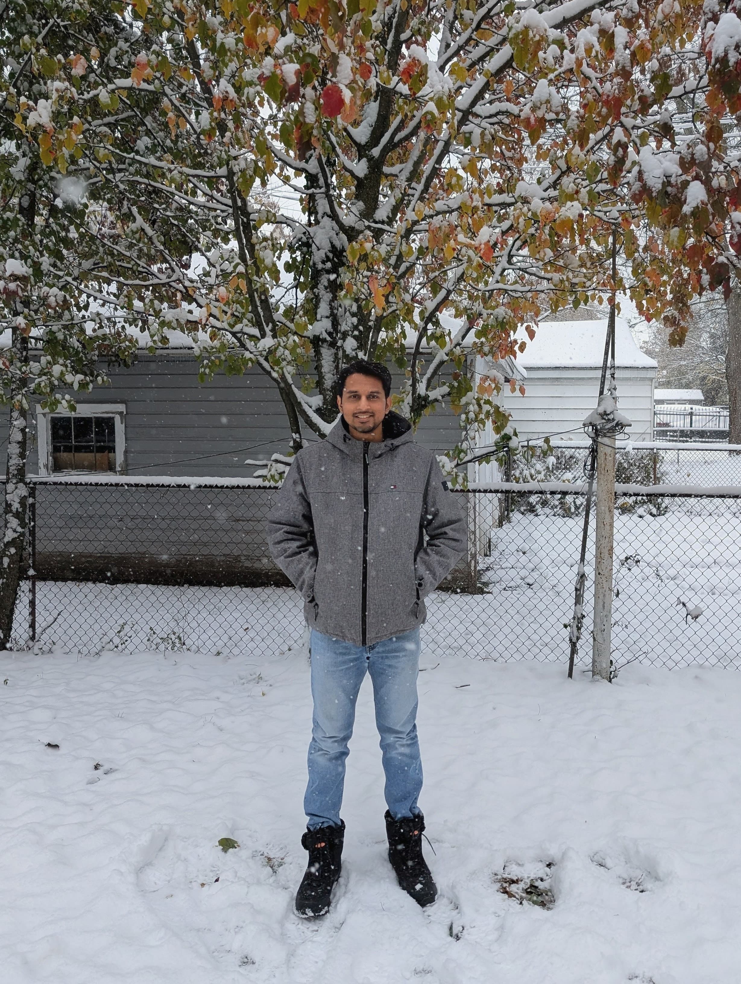 Adnan standing in fresh snow beneath a tree still holding autumn leaves