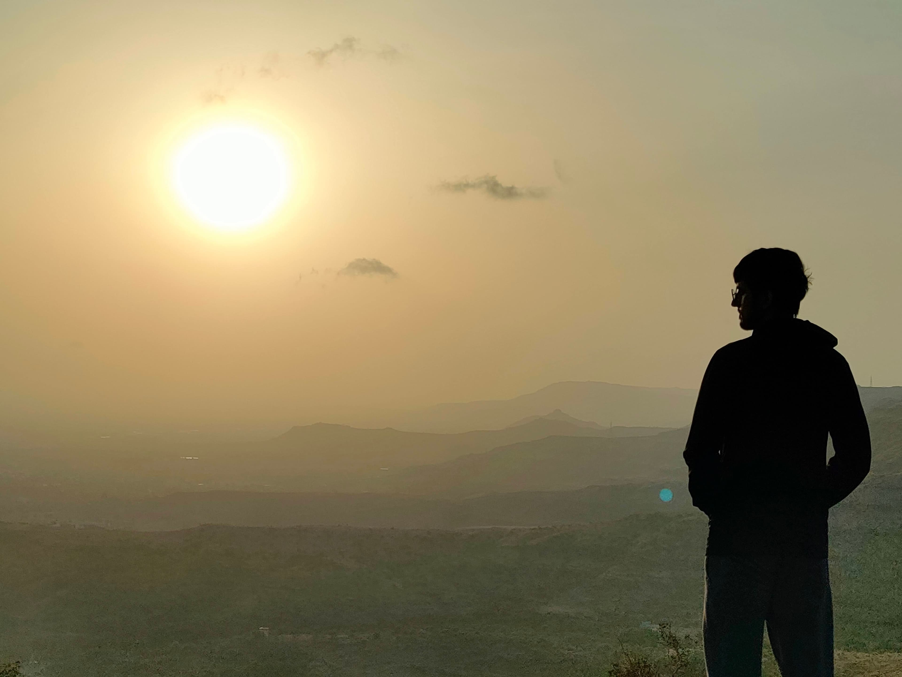 A figure silhouetted against a hazy sunset over rolling hills